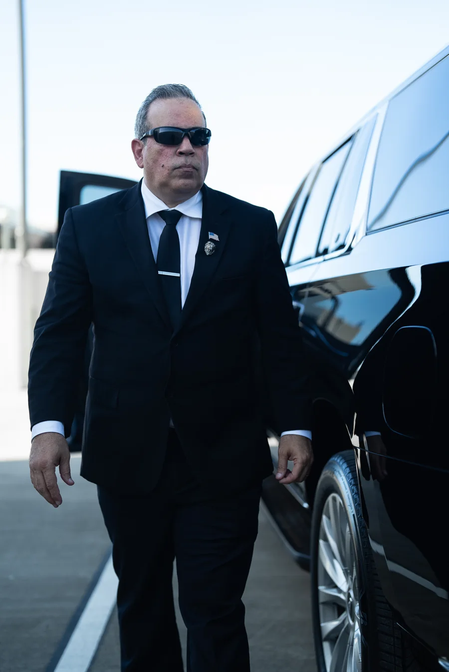 Lenox chauffeur in a black suit walking beside a black SUV